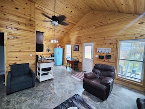 L’intérieur d’un chalet accueillant, avec un sol en pierre, des murs en bois, un réfrigérateur bleu, un canapé en cuir et un coin repas.