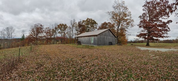 A rustic wooden barn in a rural setting with a path leading to it, surrounded by trees and fallen leaves.