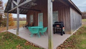 Una baita di legno con un portico coperto, un tavolo con sedie e un barbecue.