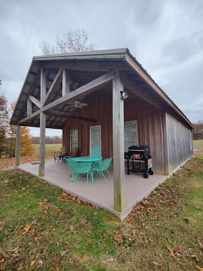 Une cabane en bois dotée d’un patio couvert, d’une table avec des chaises et d’un barbecue.