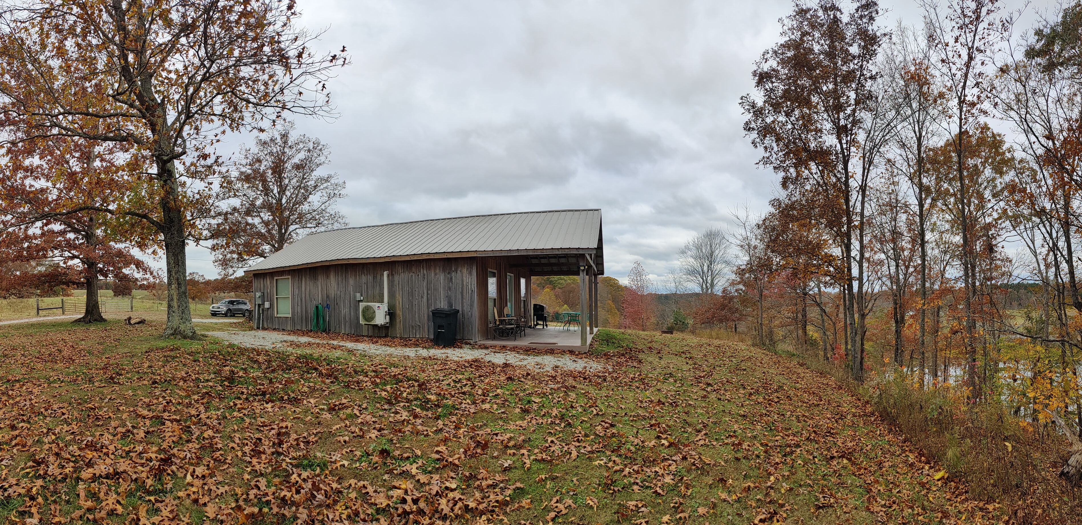 A rustic cabin with a covered porch, surrounded by trees with autumn leaves, and a gravel path leading to the entrance.