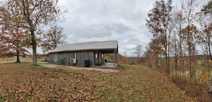 A rustic cabin with a covered porch, surrounded by trees with autumn leaves, and a gravel path leading to the entrance.