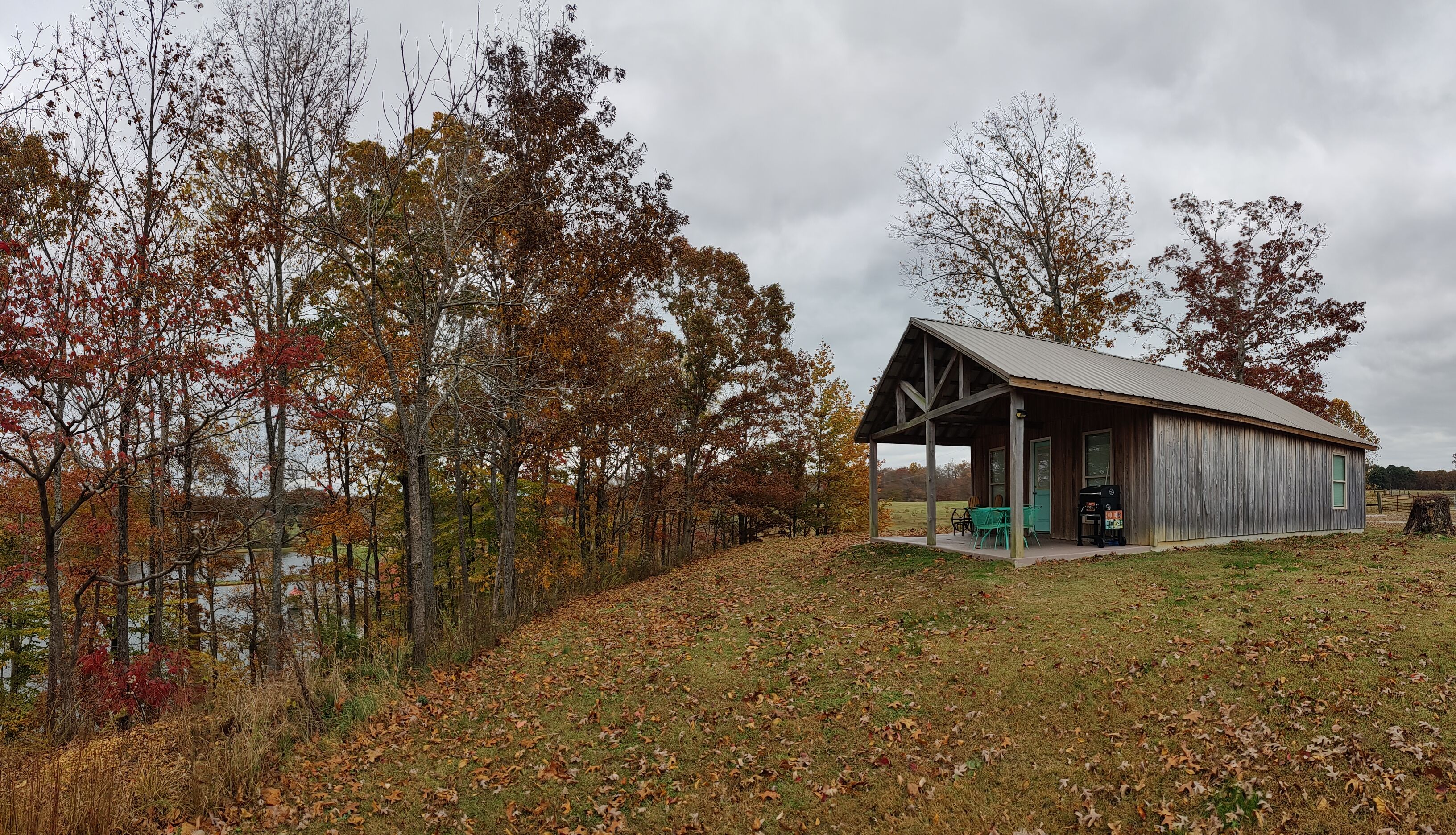 Un chalet rustique doté d’une véranda, entouré d’arbres et bordé par un plan d’eau.