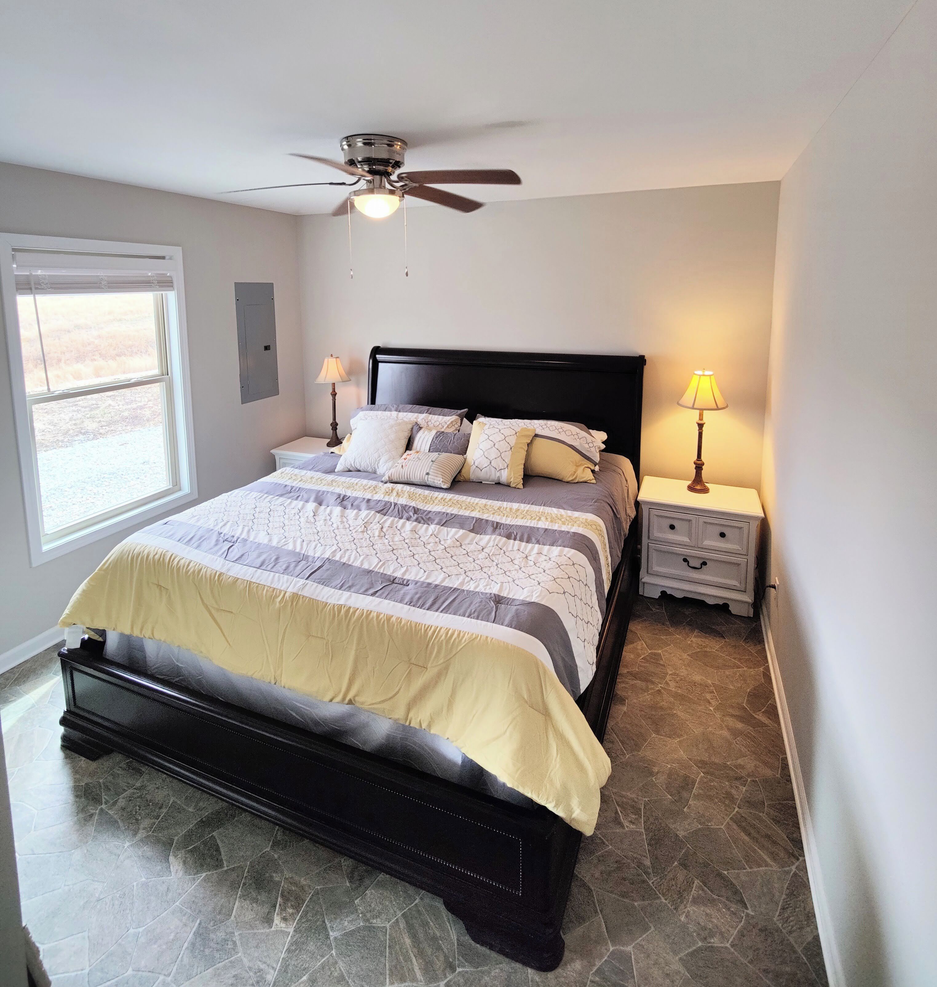 A bedroom with a bed, a ceiling fan, a nightstand, a lamp, and a window.