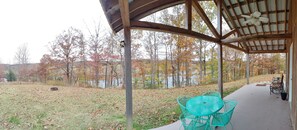 A covered outdoor area with a table and chairs, surrounded by trees and a body of water.