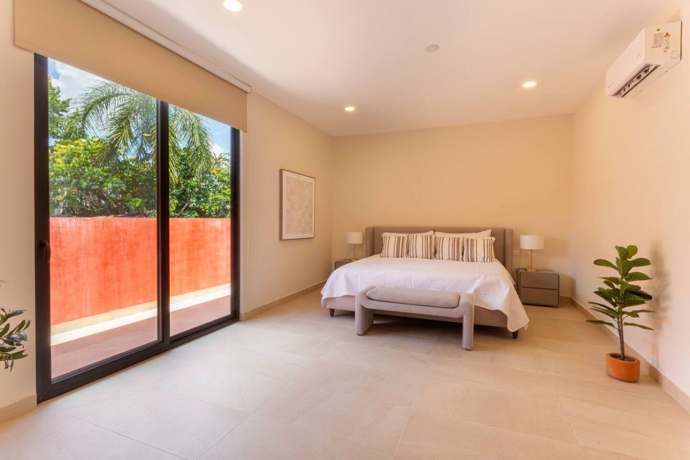 Un dormitorio con cama, mesitas de noche, ventana con vistas a la vegetación y puerta corredera.