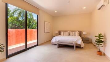 Un dormitorio con cama, mesitas de noche, ventana con vistas a la vegetación y puerta corredera.