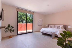 Une chambre à coucher avec un lit, une porte-fenêtre coulissante donnant sur un balcon, une plante en pot et un tableau encadré au mur.