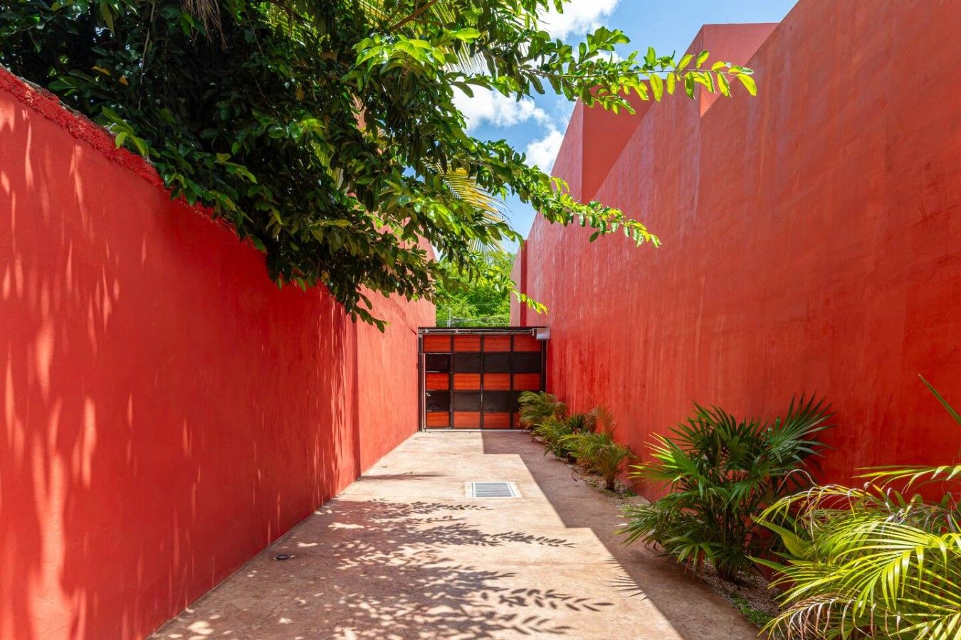 A narrow pathway flanked by red walls with a gate at the end.