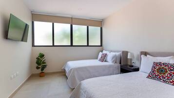 Habitación de hotel con dos camas, un televisor montado en la pared, una planta en maceta y una ventana con persianas.
