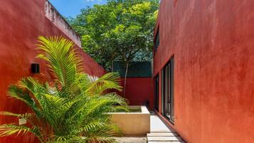 A narrow pathway flanked by red walls, leading to a building with large windows.