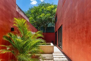 Un étroit sentier bordé de murs rouges, qui mène à un bâtiment doté de grandes fenêtres.
