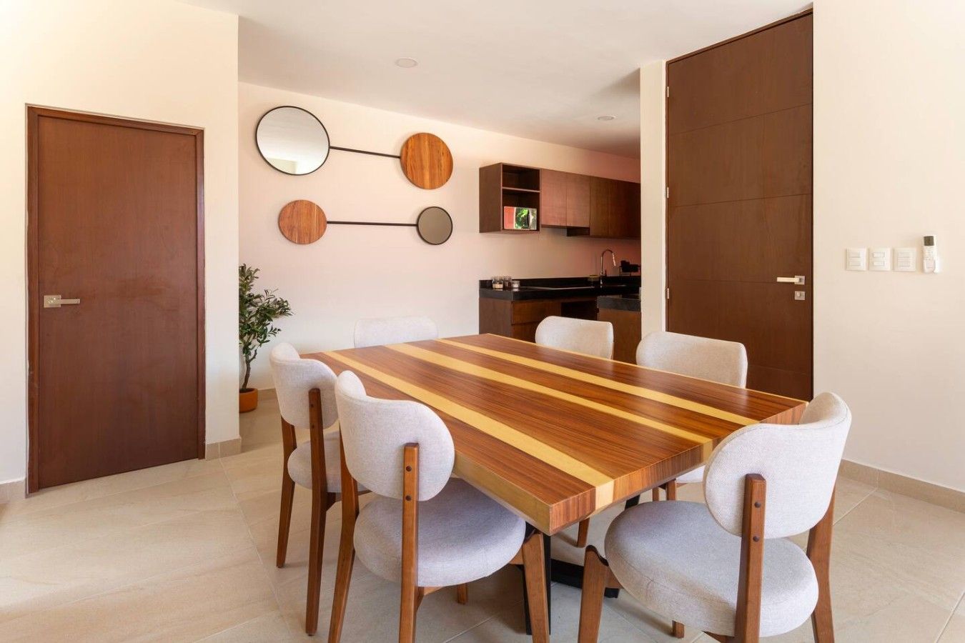 Un comedor con una mesa de madera y seis sillas, una cocina al fondo y una puerta a la izquierda.