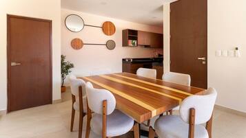 Un comedor con una mesa de madera y seis sillas, una cocina al fondo y una puerta a la izquierda.