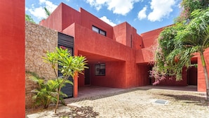 Un edifici modern amb façana vermella, mur de pedra i un pati pavimentat amb lladrics.