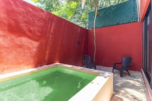 Ein kleiner Poolbereich im Freien mit zwei Stühlen, umgeben von roten Wänden und einem grünen Zaun.