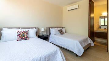 Habitación de hotel con dos camas, una mesita de noche, una lámpara, un equipo de aire acondicionado y un baño con espejo y lavamanos.