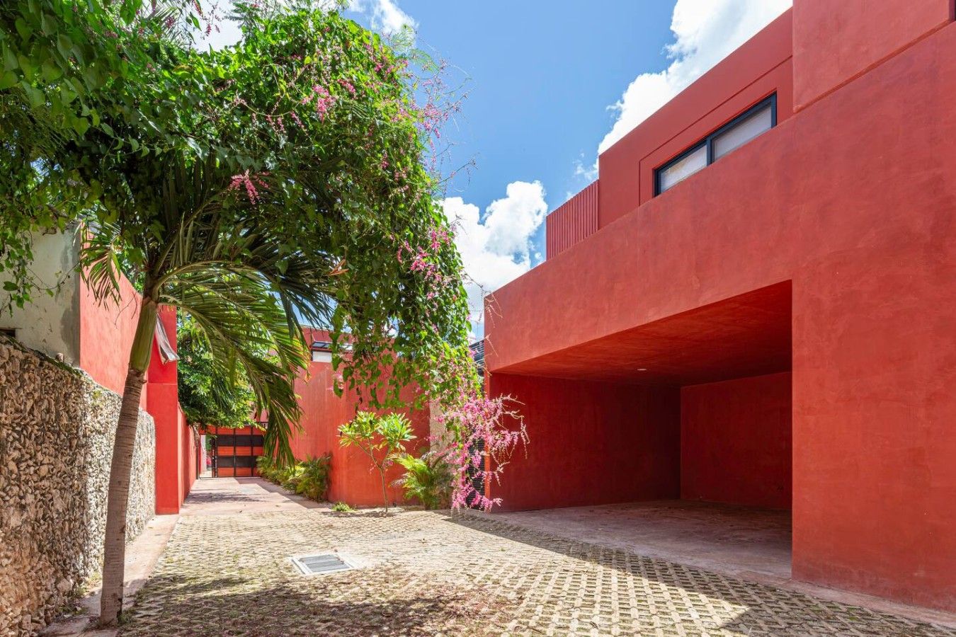 Un patio con un edificio rojo, una palmera y plantas con flores.