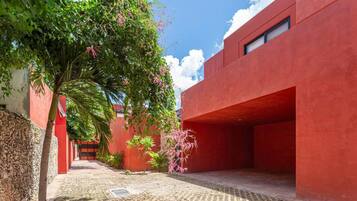Un patio con un edificio rojo, una palmera y plantas con flores.