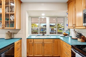 A kitchen with wooden cabinets, a window with a view of the outdoors, a sink, and various kitchen items. - Waterfront Oasis • Heated Pool & Spa • Near Beach (Oakland Park)