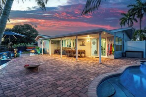 A modern outdoor patio with a pool, a covered seating area, and a sunset view. - Waterfront Oasis • Heated Pool & Spa • Near Beach (Oakland Park)