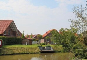 A residential area with houses, a small pond, and a white fence. - Holiday Apartment in Greetsiel With Terrace (Krummhoern)