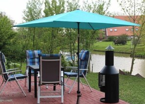 An outdoor patio with a grill, chairs, and a table under a blue umbrella. - Holiday Apartment in Greetsiel With Terrace (Krummhoern)