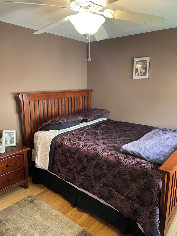 A bedroom with a wooden bed, a nightstand, a framed picture, and a ceiling fan.