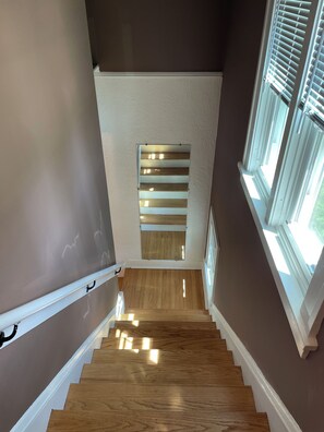 A staircase with wooden steps and white handrails, leading to a landing with a window and a small wooden panel.