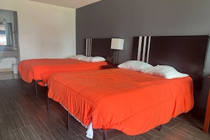 Quarto de hotel com duas camas, cada uma com colcha vermelha e almofadas brancas.