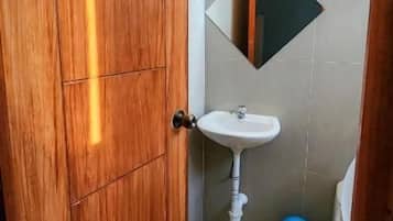 Un baño con puerta de madera, un lavabo, un espejo y un cubo azul.