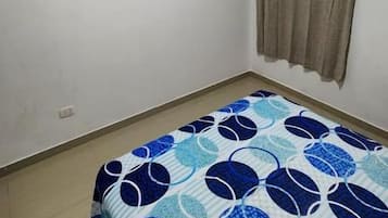 Un dormitorio con cama, ventilador de techo, televisor y ventana con cortinas.