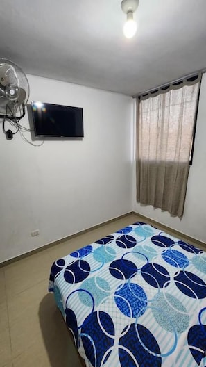 A bedroom with a bed, a ceiling fan, a television, and a window with curtains. - VALLE DEL SOL HOTEL (Ica)