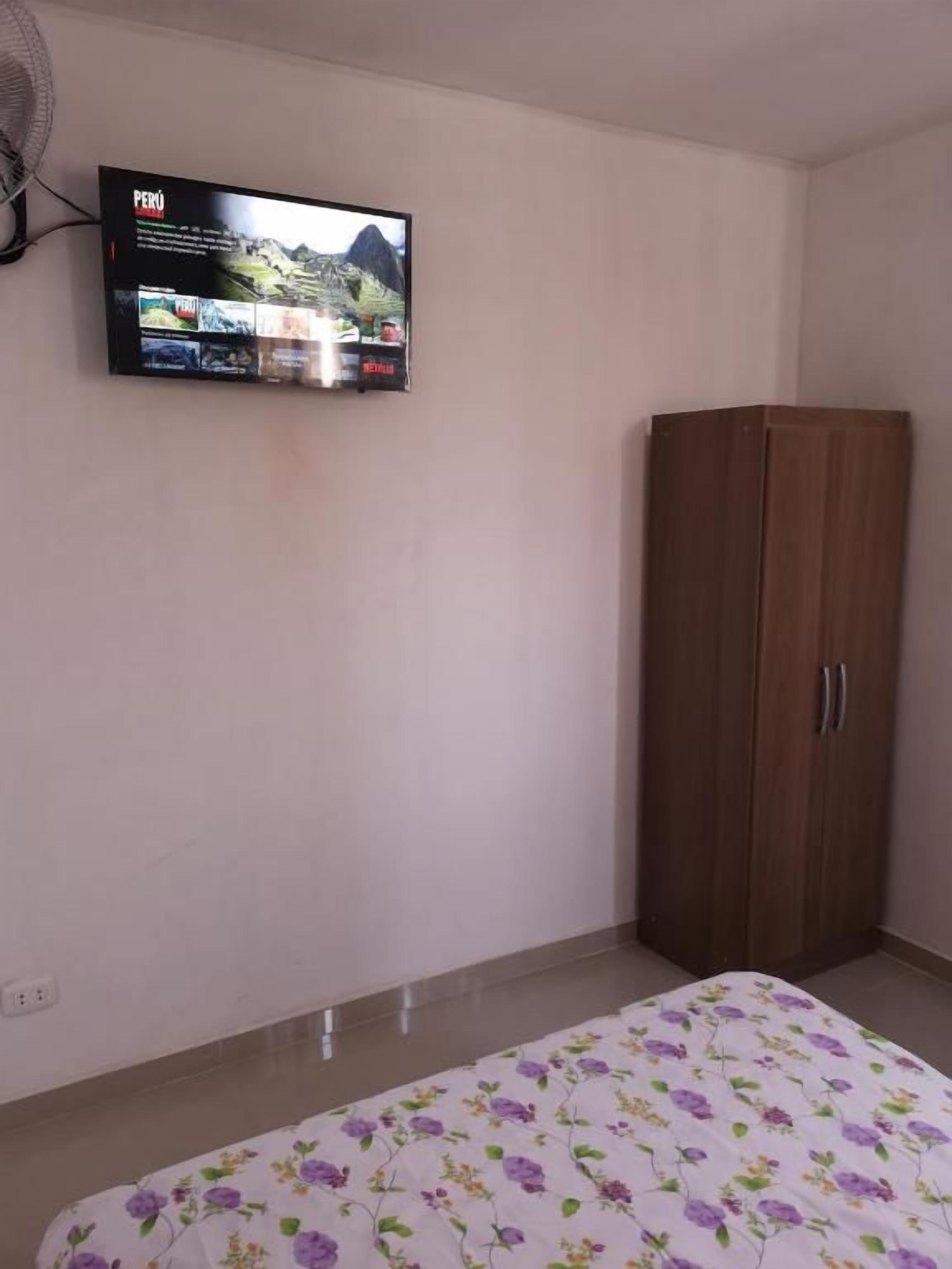 Un dormitorio con cama, armario y televisor de pared mostrando un programa de viajes.