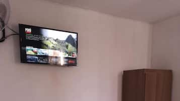 Un dormitorio con cama, armario y televisor de pared mostrando un programa de viajes.