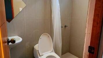 A small bathroom with a toilet, a shower curtain, and a blue trash bin.