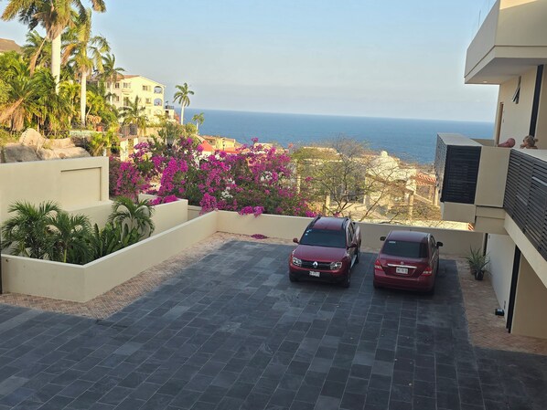 Ein Parkplatz mit zwei Autos, Blick aufs Meer und ein Gebäude mit Balkon.