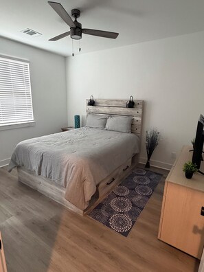 A bedroom with a bed, a ceiling fan, a nightstand, a dresser, a window with blinds, and a patterned rug. - Katy Comfort Townhome (Katy)