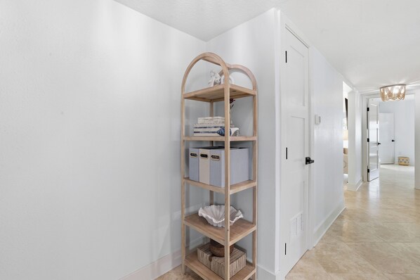 Un couloir avec une étagère en bois adossée à un mur blanc, qui mène à une porte.