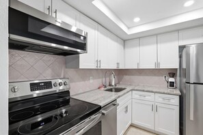 Une cuisine moderne dotée d’appareils électroménagers en acier inoxydable, de meubles blancs et d’un four encastré.