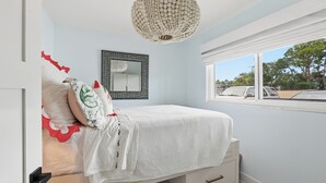 Ein Schlafzimmer mit einem Bett, einer Pendelleuchte, einem Fenster und einem Spiegel an der Wand.