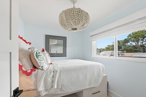 Um quarto com uma cama, luminária pendente, janela e espelho na parede.