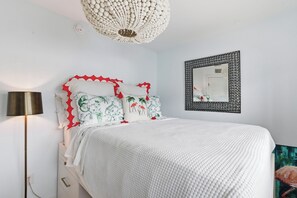 Une chambre à coucher comprenant un lit, une lampe de chevet, un miroir fixé au mur et un luminaire au plafond.
