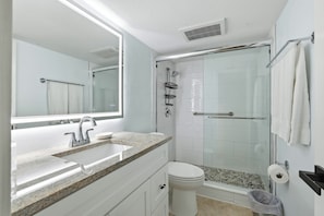 Casa de banho moderna com lavatório de bancada de granito, sanita e cabine de duche com vedação de vidro, além de um espelho grande.