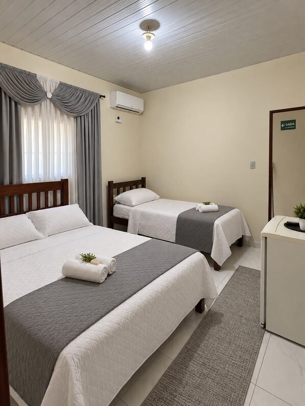 Quarto de hotel com duas camas, uma escrivaninha, um espelho e uma janela com cortinas.