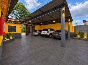 Uma área de estacionamento coberta com três carros estacionados, um hidrante e um edifício com fachada amarela.