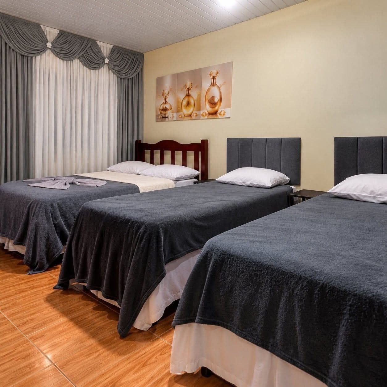 A hotel room with three beds, wooden headboards, and a painting on the wall.
