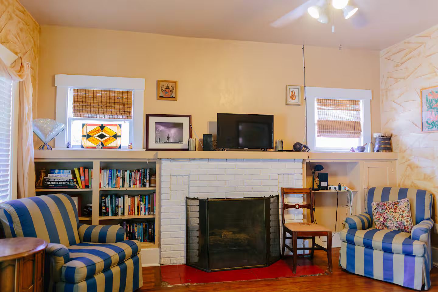 A cozy living room with a fireplace, striped armchairs, a bookshelf, and a television.