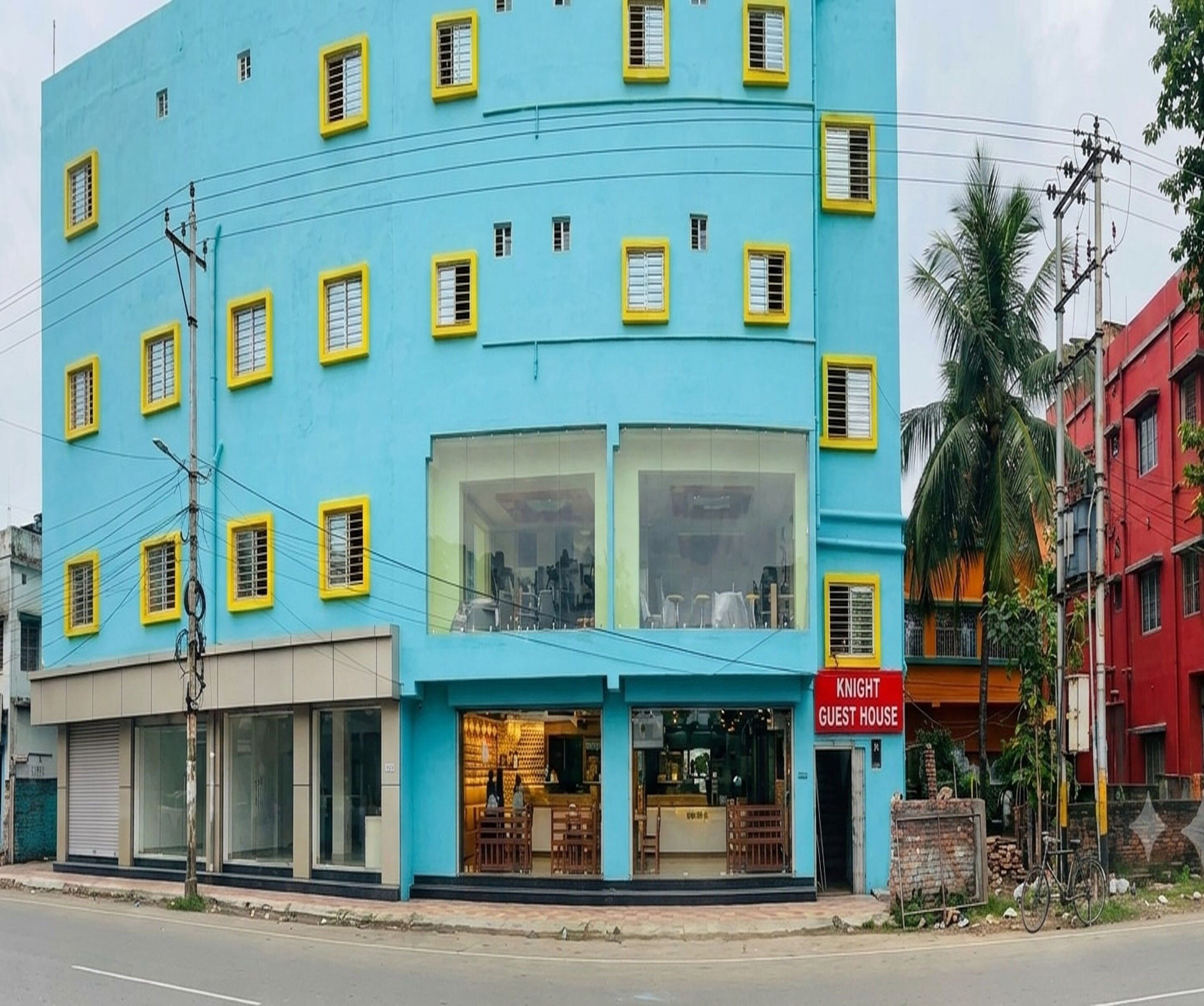 Un edificio de varios pisos con fachada azul y marcos de ventana amarillos, que cuenta con un restaurante en la planta baja con mesas visibles y un letrero que dice 'KNIGHT GUEST HOUSE'.