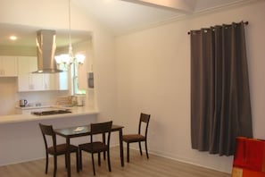 A dining area with a table and chairs, a kitchen in the background, and a curtain on the window. - Clean, comfortable, quiet and affordable accommodation in Rosenberg (Rosenberg)
